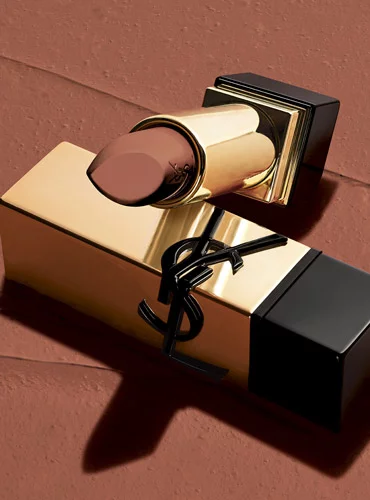 A gold YSL lipstick with a brown shade on a brown background.