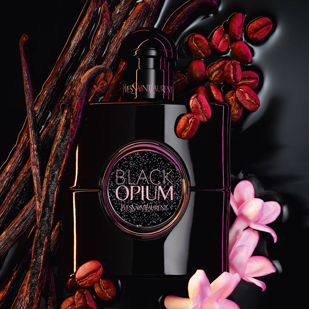 YSL Black Opium perfume bottle surrounded by vanilla beans, coffee beans, and pink flowers.