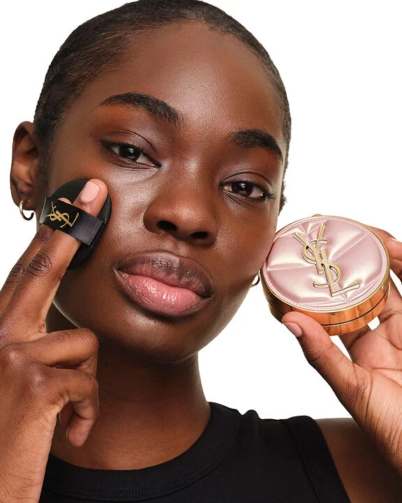 Model with deep skin tone holding the YSL SKIN AFFAIR SOFT GLOW CUSHION. Radiant, unified and healthy-looking glow.