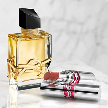 YSL perfume bottle and two lipsticks on a marble surface.
