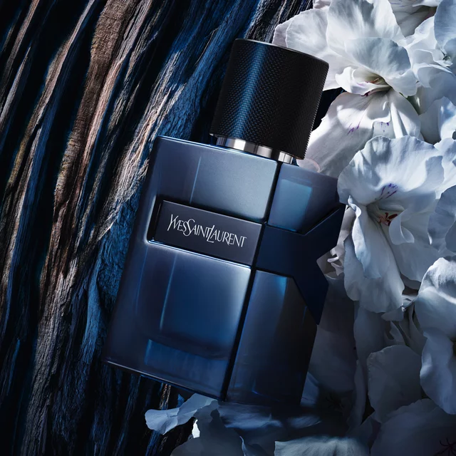 YSL perfume bottle with dark blue liquid and a black cap, placed next to white flowers and wood.