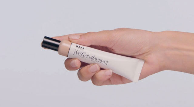 A hand holding a tube of YSL Nu foundation.