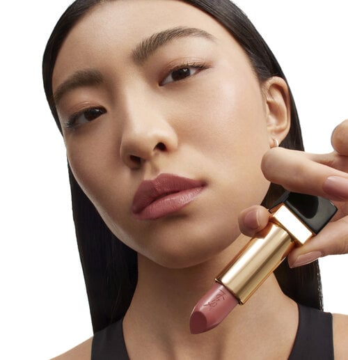 A woman holding a gold YSL lipstick near her face.