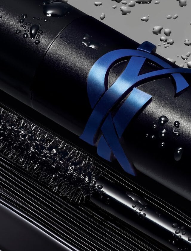 Close-up of a black mascara tube with a blue ribbon and water droplets.