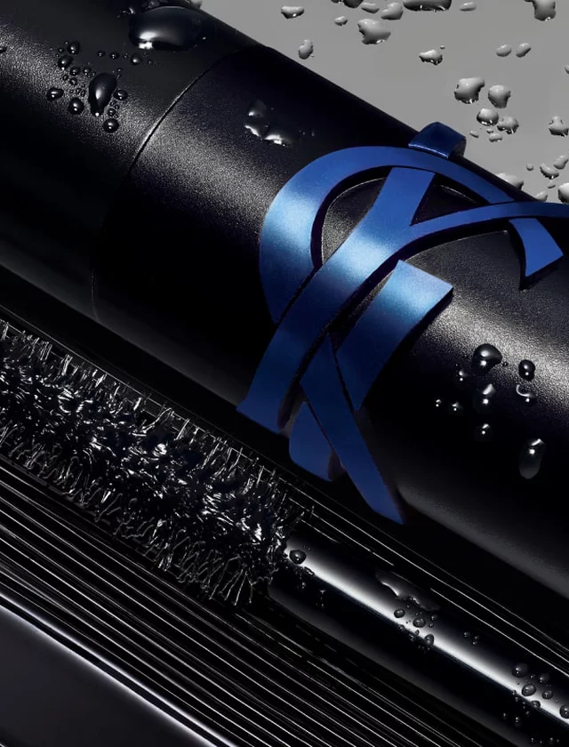 Close-up of a black mascara tube with a blue ribbon and water droplets.