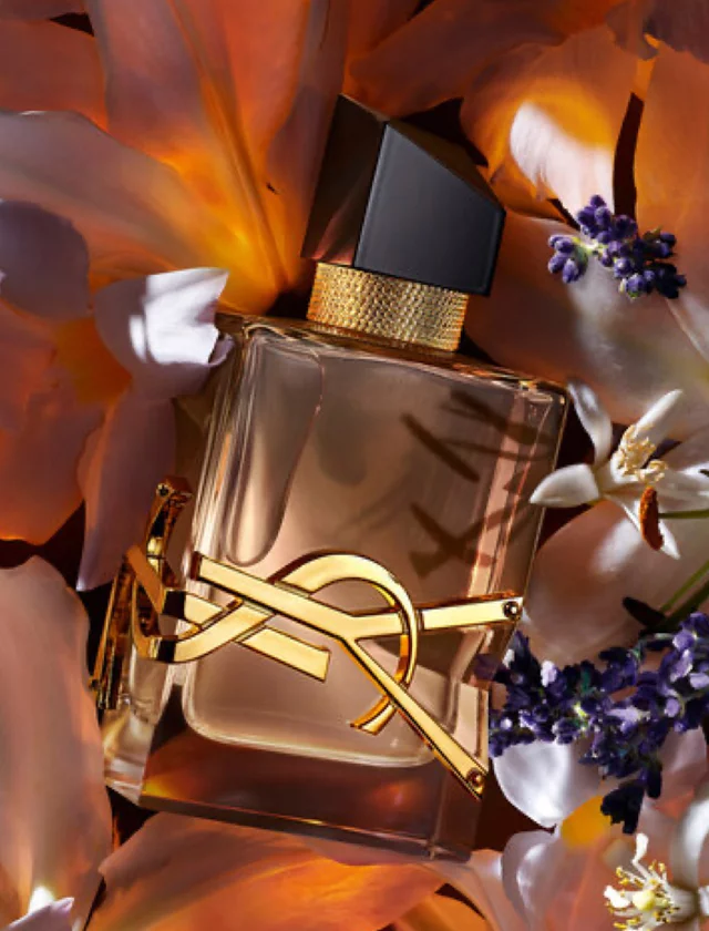 YSL perfume bottle with amber liquid surrounded by orange and white flowers.