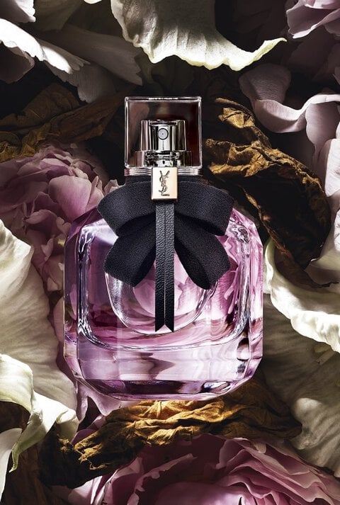 YSL perfume bottle with a black bow, surrounded by white and pink flowers.