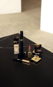 YSL makeup products including foundation, mascara, lipstick, and eyeshadow on a black surface.