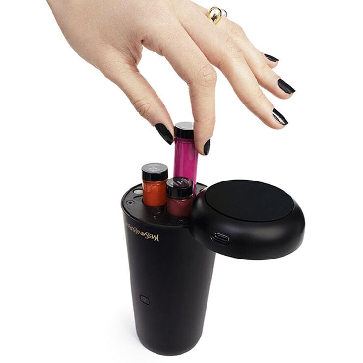Hand with black nail polish placing a pink vial into a black Yves Saint Laurent device.