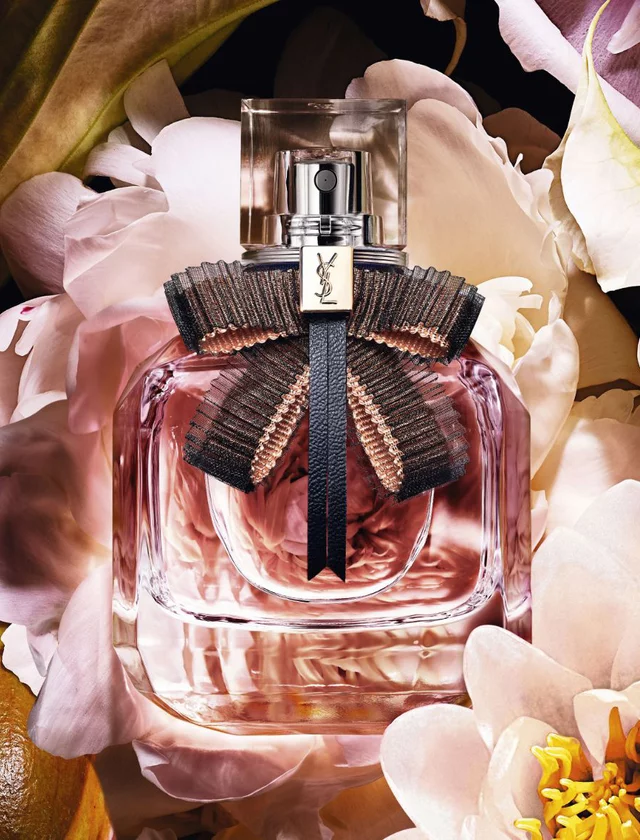 YSL perfume bottle with pink liquid and a black bow, surrounded by pink flowers.