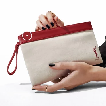 Hands holding a beige and red YSL clutch bag.