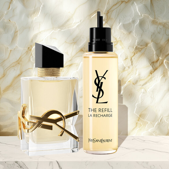 Two YSL perfume bottles, one with amber liquid and the other labeled 'THE REFILL LA RECHARGE,' on a marble surface.