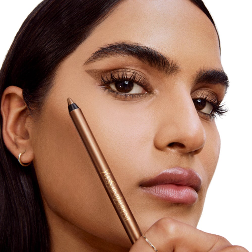 A person holding a YSL eye pencil next to the golden brown hue applied to their eyes