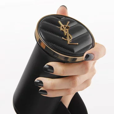 A hand holding a black cylindrical YSL product with a gold and black lid.