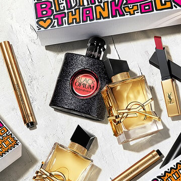 A collection of YSL beauty products including Black Opium and other perfumes, lipstick, and a thank you card.