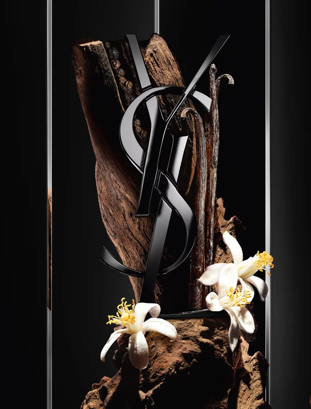 YSL logo with white citrus flowers and wood on a black background.