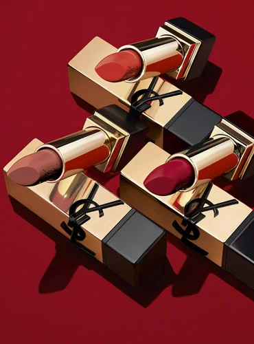 Three YSL lipsticks in gold cases with different shades on a red background.