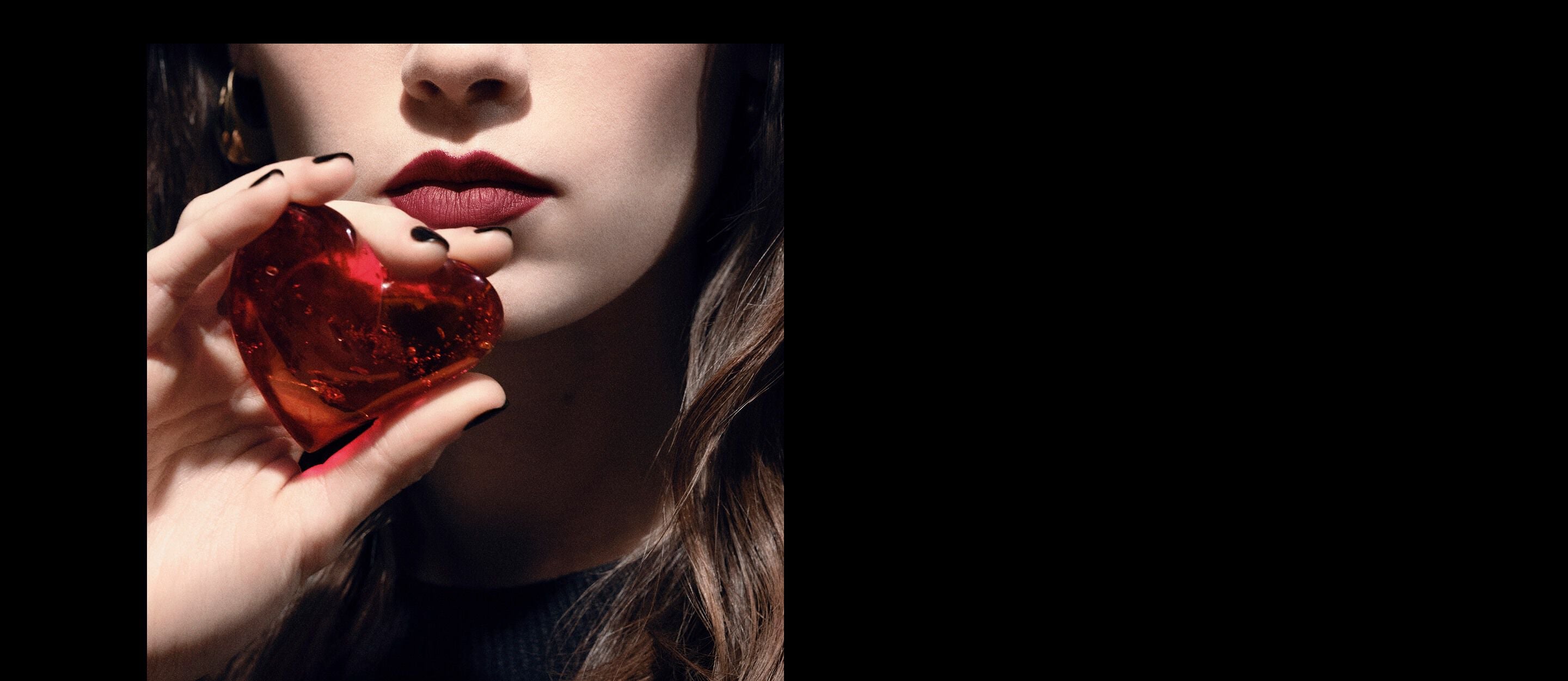 Close-up of a model's lips and hand
holding a translucent ruby-red heart
jewel for YSL CŒUR Eau de Parfum.