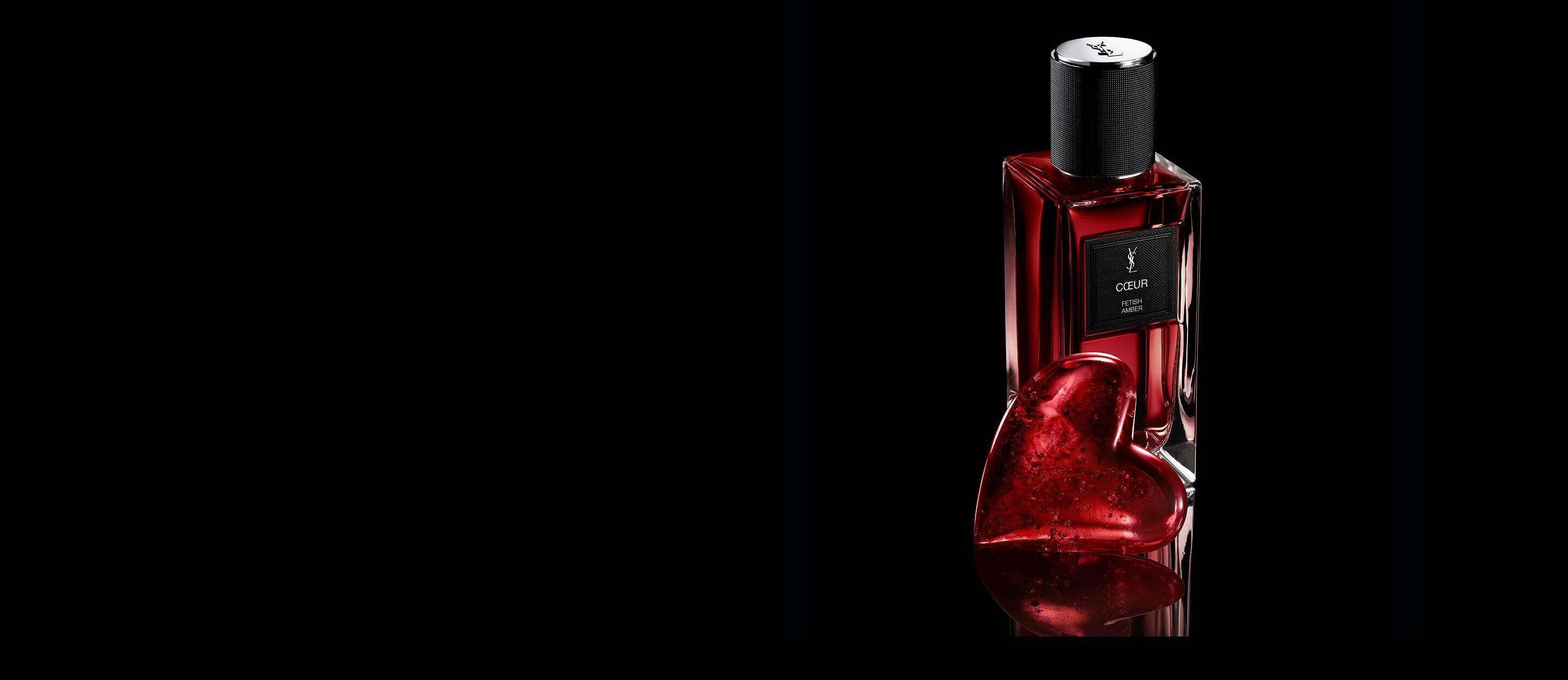 CŒUR Eau de Parfum by YSL bottle
next to a ruby-red heart jewel on a
reflective black surface.